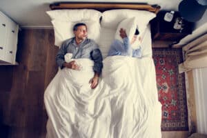 A woman covering her ears while her husband with sleep apnea snores