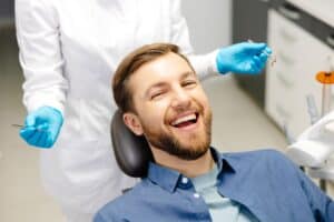A man sitting in a dentist's chair and smiling after getting a dental bridge